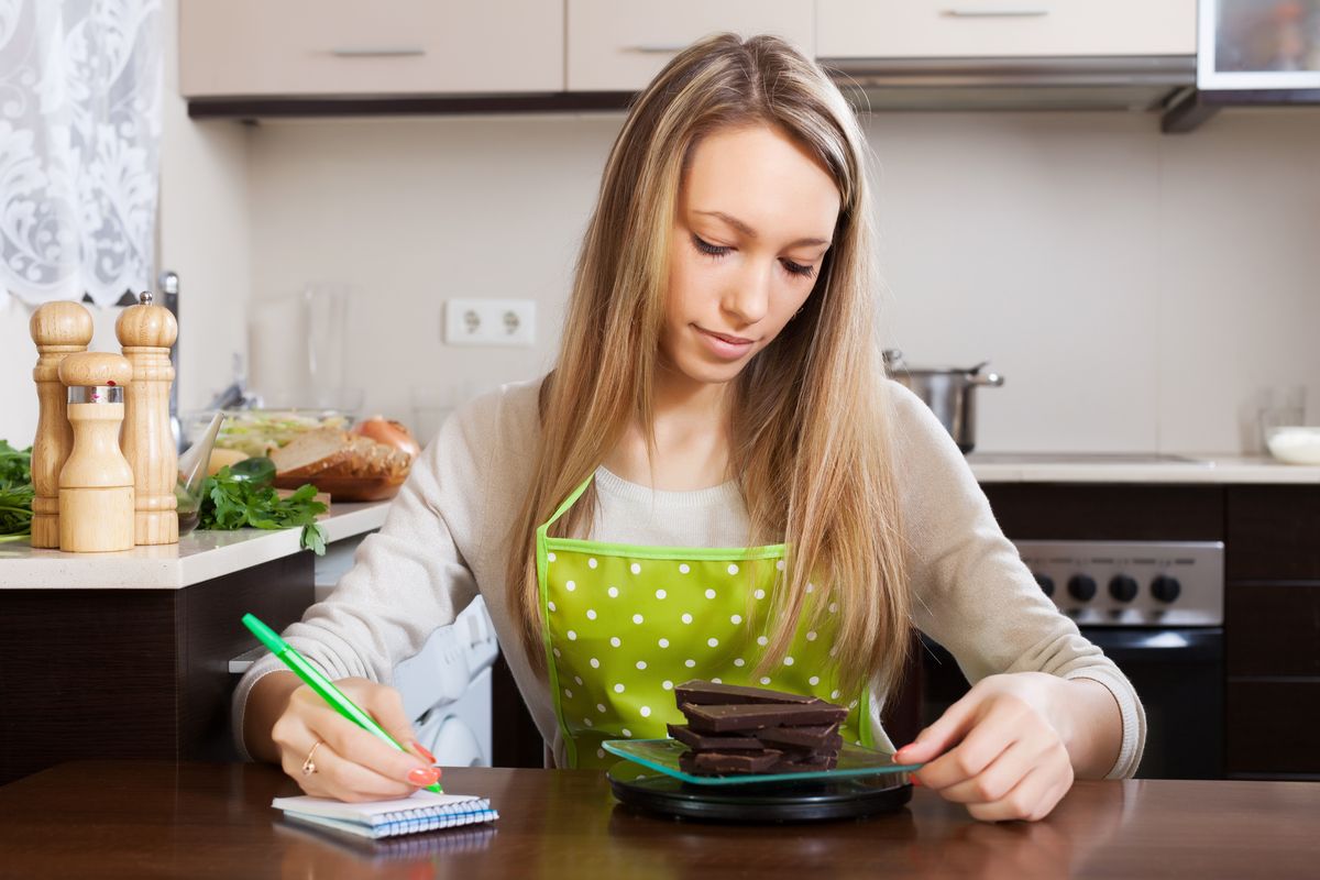 Femme qui pèse ses aliments dans une cuisine avec une balance de cuisine pas chère.